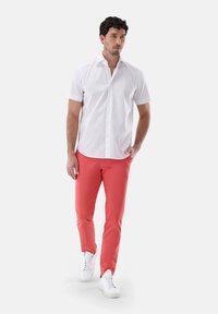 Weißes Kurzarmhemd mit feinem Karomuster, kombiniert mit eng anliegenden korallfarbenen Hosen und weißen Sneakers, die ein lässiges Outfit ergeben.