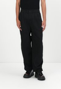 Black, loose-fitting trousers with a high waist, elastic waistband, and button closure. Made from soft fabric, featuring straight legs and no visible patterns.