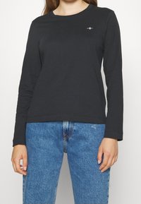 Zwarte longsleeve t-shirt van katoen, met een ronde halslijn en subtiele logo op de borst, gecombineerd met blauwe denim jeans.
