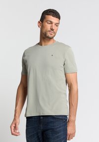 Lichtgroene t-shirt met korte mouwen van zachte katoen, ronde hals, met een klein logo op de borst, gedragen met blauwe spijkerbroek.