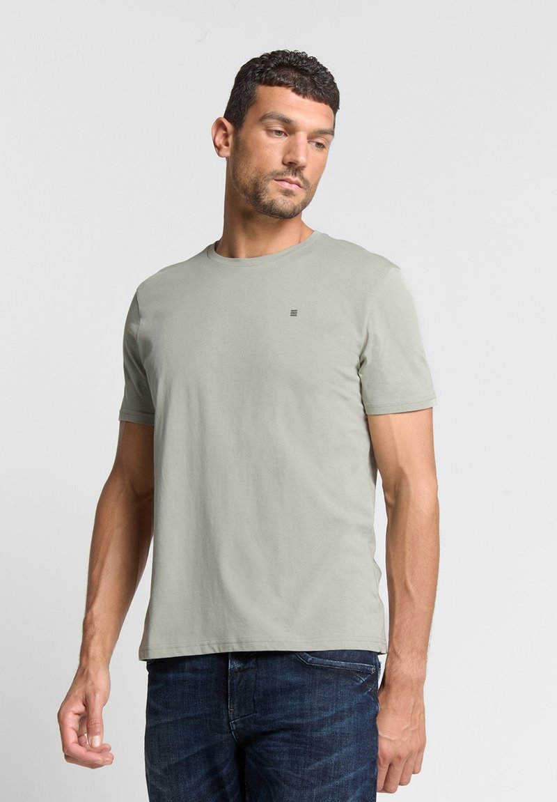 Lichtgroene t-shirt met korte mouwen van zachte katoen, ronde hals, met een klein logo op de borst, gedragen met blauwe spijkerbroek.