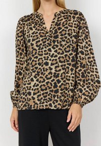Blouse en imprimé léopard beige et noir, avec un col en V, des manches longues bouffantes et un tissu texturé avec un léger éclat.