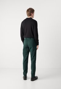 Pantalones verdes ajustados con una textura suave y un frente plano, combinados con una camiseta negra de manga larga. Diseño simple, sin patrones visibles.