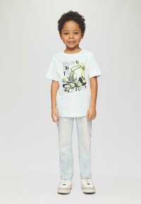 Weißes Baumwoll-T-Shirt mit einem Bagger-Graphic und Text, kombiniert mit hellblauen Jeans und weißen Schuhen mit grauen Akzenten.