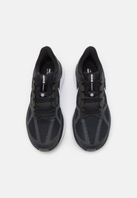Scarpe da ginnastica Nike nere con parte superiore in rete, dettagli testurizzati, accenti bianchi e lacci neri. Suola spessa bianca con battistrada visibile.