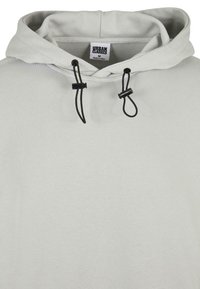 Sudadera gris con capucha y cordones. Presenta detalles negros y una etiqueta que dice "URBAN CLASSICS". El material parece suave y con textura.