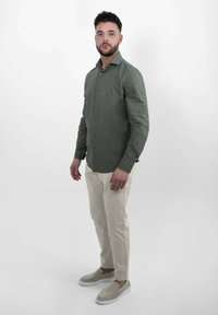 Overhemd met knopen in olijfgroene stof, slim fit met lange mouwen en een kraag, gecombineerd met crèmekleurige broeken en lichtkleurige instappers.
