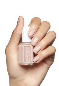 Bouteille de vernis à ongles avec un capuchon blanc, tenue dans une main. Le vernis à ongles est d'une teinte beige douce, finition brillante, avec de courts ongles bien manucurés.