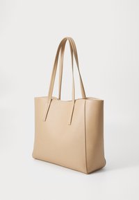 Sac fourre-tout en cuir beige avec deux longues poignées, forme structurée, texture lisse et coutures minimales. Aucun matériel ou accent visible.