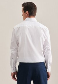 Biała koszula z długim rękawem i klasycznym kołnierzykiem, z zapięciem na guzik przy mankietach i gładką strukturą, zestawiona z granatowymi spodniami.