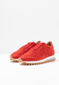 Punaiset mokkanahka sneakersit, joissa on pyöreä kärki, nauhakiinnitys ja kumipohja, jossa on kuvioitu pito. Vastaava valkoinen välipohja.