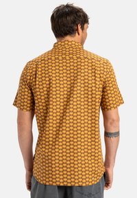Short-sleeve shirt in yellow and brown geometric pattern with a straight hem and folded collar. Made from lightweight fabric with a smooth texture.