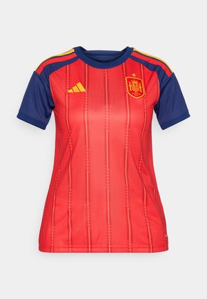 Červený futbalový dres s námorníckymi modrými rukávmi, s pruhovaným dizajnom a zlatými akcentmi. Logo Adidas a emblém Španielska sú zreteľne zobrazené.