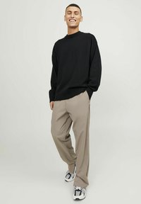 Czarny oversize sweter z prążkowanym dekoltem, w połączeniu z jasnobeżowymi spodniami w kant i czarno-białymi sneakersami. Casualowy fason.