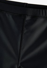 Shorts de bain noirs en matériau lisse, dotés d'une ceinture plate et de coutures flatlock pour le confort et la durabilité.