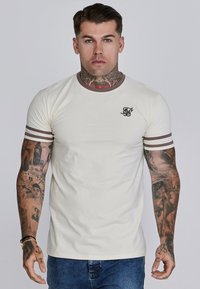 Crème t-shirt met bruine kraag en mouwstrepen, voorzien van een klein zwart logo op de borst. Getailleerd ontwerp gemaakt van een zachte katoenmix.