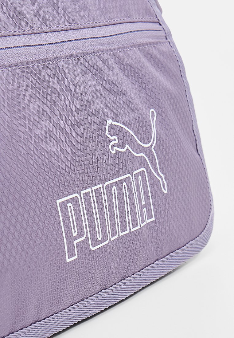 Bolsa de tela morada con cierre de cremallera, patrón de diamantes texturizado y logo blanco de Puma exhibido de manera prominente.