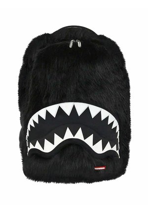 Mochila negra peluda con un bolsillo delantero que presenta un diseño de boca de tiburón con dientes irregulares en blanco y tiradores de cremallera plateados.