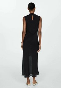 Zwarte mouwloze jurk met een hoge hals en sleutelgatenrugdetail. Gemaakt van lichtgewicht stof, heeft het een vloeiende silhoeet en een lengte tot de knie.