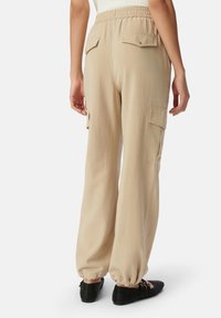 Beige cargobroek met een elastische tailleband, voorzien van twee achterzakken en elastische boorden bij de enkels. Zachte stoftextuur.