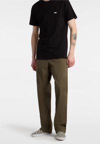 T-shirt nera a maniche corte con logo bianco, pantaloni dritti verde oliva, e scarpe slip-on a scacchi bianco e nero.