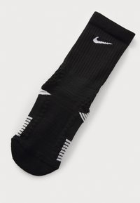 Sort sportsok med ribbet tekstur, hvidt Nike-logo og hvide stribede detaljer på manchet og sider.