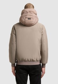 Puhított bézs dzseki nagyméretű, steppelt kapucnival. Bordás mandzsetták és derékpánt. Simább szövet textúra minimális márkázással a hátsó részen.