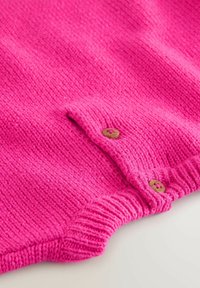 Tessuto lavorato a maglia di un vivace rosa con due piccoli bottoni di legno e un bordo a costine, probabilmente parte di un indumento o di un accessorio.