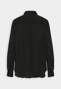 Chemise noire à manches longues avec un col, une texture lisse, un empiècement au dos et des poignets boutonnés, présentant une coupe décontractée.