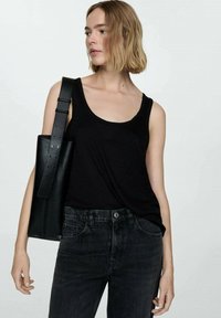 Black sleeveless tank top made from soft fabric, paired with dark denim jeans. The model carries a structured black tote bag with a long strap.