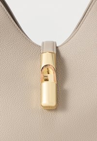 Τσάντα χειρός από μπεζ δέρμα με χρυσό μεταλλικό κούμπωμα σε σχήμα κύκλου, με λεία υφή και στρογγυλεμένο επάνω μέρος.