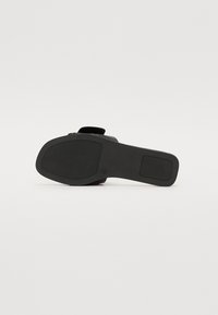 Chaussure plate noire avec une tige texturée et une semelle en caoutchouc lisse. Le design présente une large lanière et une semelle intérieure rembourrée pour plus de confort.
