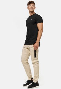 Czarny t-shirt z krótkim rękawem z małym logo, w połączeniu z beżowymi spodniami z czarną boczną kieszenią i teksturowanym materiałem. Całość uzupełniają czarne sneakersy.
