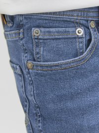 Jeans de ganga azul com costuras visíveis, dois bolsos frontais e detalhes em metal nas bordas dos bolsos.