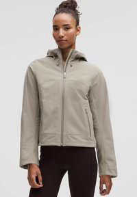 Jachetă zip-up de culoare gri deschis, cu glugă, având cusături plate, o textură netedă, buzunare laterale și șnururi ajustabile pe glugă.