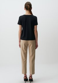 Czarny t-shirt z krótkim rękawem o luźnym kroju, zestawiony z beżowymi spodniami na miarę i czarnymi sandałami na obcasie, widok od tyłu.