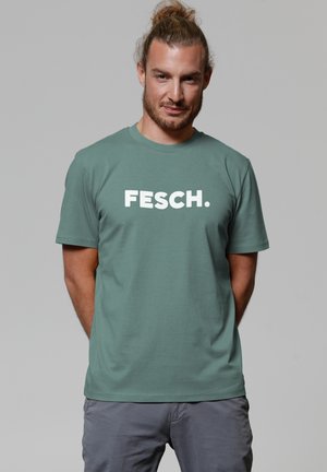 Groene katoenen t-shirt met de opvallende witte tekst "FESCH." Ronde hals, korte mouwen en een relaxte pasvorm. Zachte textuur.