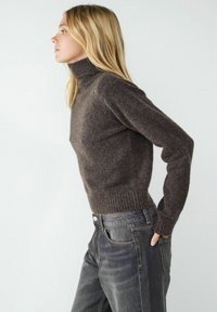 Brauner, gestrickter Rollkragenpullover mit geripptem Saum und Bündchen, kombiniert mit dunklen Denim-Jeans. Der Pullover hat eine weiche Textur und eine taillierte Passform.