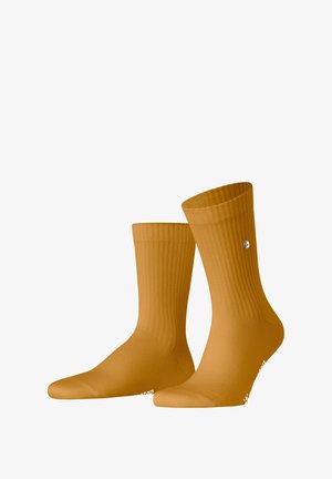 Chaussettes jaunes côtelées avec un poignet ajusté et un doigt de pied renforcé. Présente un petit logo près de la cheville. Le matériau semble lisse et extensible.