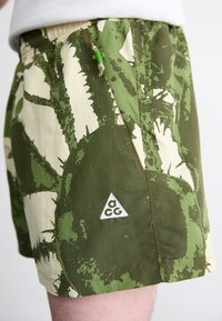 Herreshorts i et grønt og creme camouflage mønster, fremstillet af letvægtsstof. Har et lille logo patch og en lynlåslomme på siden.
