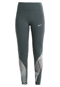 Leggings a vita alta in tessuto verde scuro con logo Nike bianco. Pannello laterale distintivo con motivo a strisce diagonali nere e bianche.