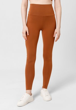 Bruine high-waisted leggings gemaakt van rekbaar stof, met een gladde textuur en een aansluitend ontwerp, gecombineerd met witte sneakers.