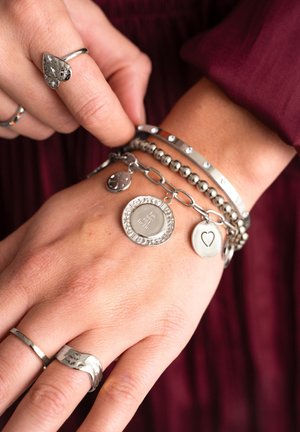 Anillos y pulseras de plata con diversos diseños en una mano. Las características incluyen encantos texturizados, bandas lisas y eslabones redondos.