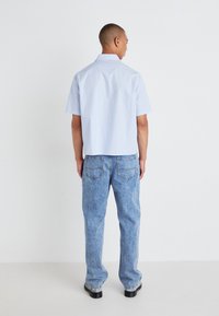Chemise à manches courtes bleu clair avec une coupe décontractée, associée à un jean en denim délavé avec deux poches arrière et une coupe droite.