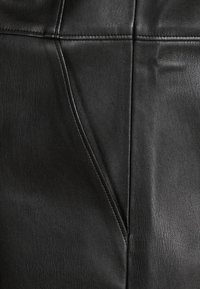Tissu en cuir noir affichant une surface texturée avec des coutures et des seams visibles. Présente une finition lisse et légèrement brillante.