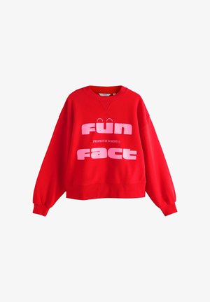 Punane särgiga särk, millel on ringkrae, üle suurte varrukate ja julge roosa tekstiga "LÕBUS FAKT." Omadused on ribaga allservas ja varrukatöös.