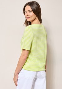 Zeleno-bíle pruhovaná krátká košile s kulatým výstřihem a volným střihem, vyrobená z lehkého materiálu. Jednoduchý design na zádech.