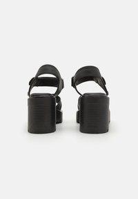Svarte plattformsandaler med tykke, strukturerte hæler, brede ankelremmer og justerbare spenner. Glatt skinnmateriale.