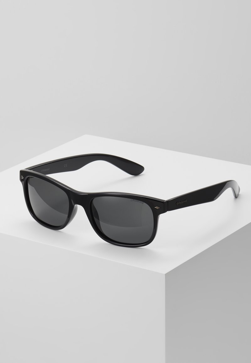 Ochelari de soare din plastic negru cu lentile gri, având un cadru rectangular și temple curbate. Logo-ul este afișat pe lateral.