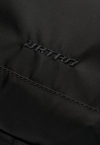 Black textile featuring a subtle ribbed texture. Embroidered logo in black thread and visible stitching detail.